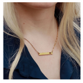 Gold necklace with a bar pendant on a person.